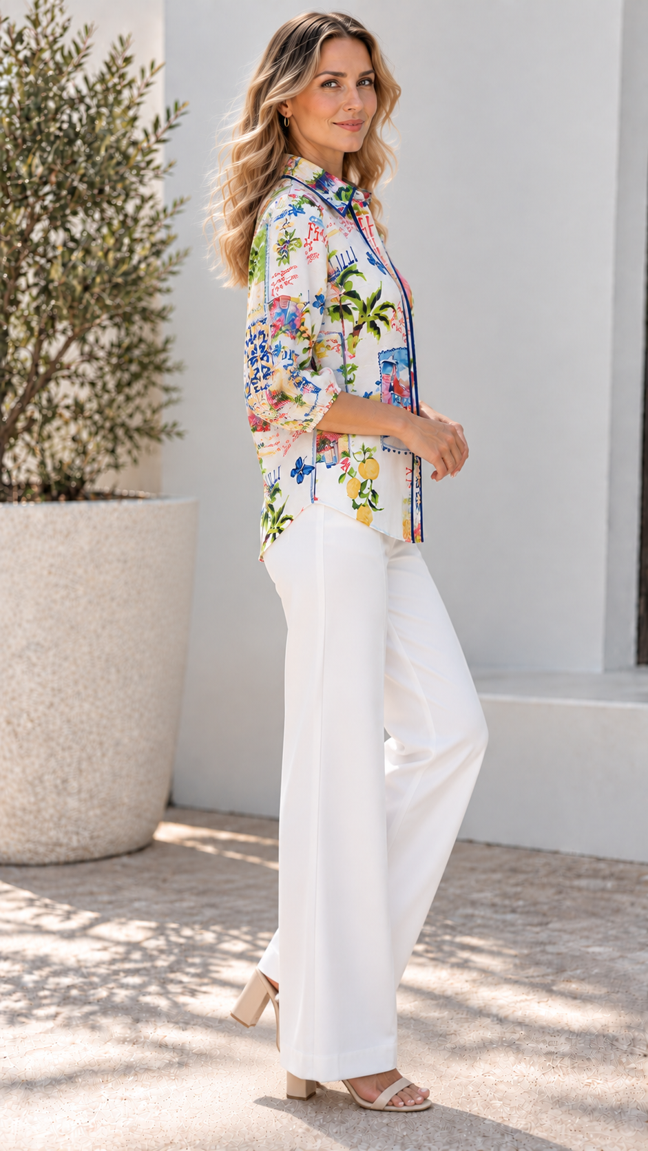 Woman wearing a colorful Italy print Bella Shirt with lemons and landmarks, paired with white wide-leg trousers.