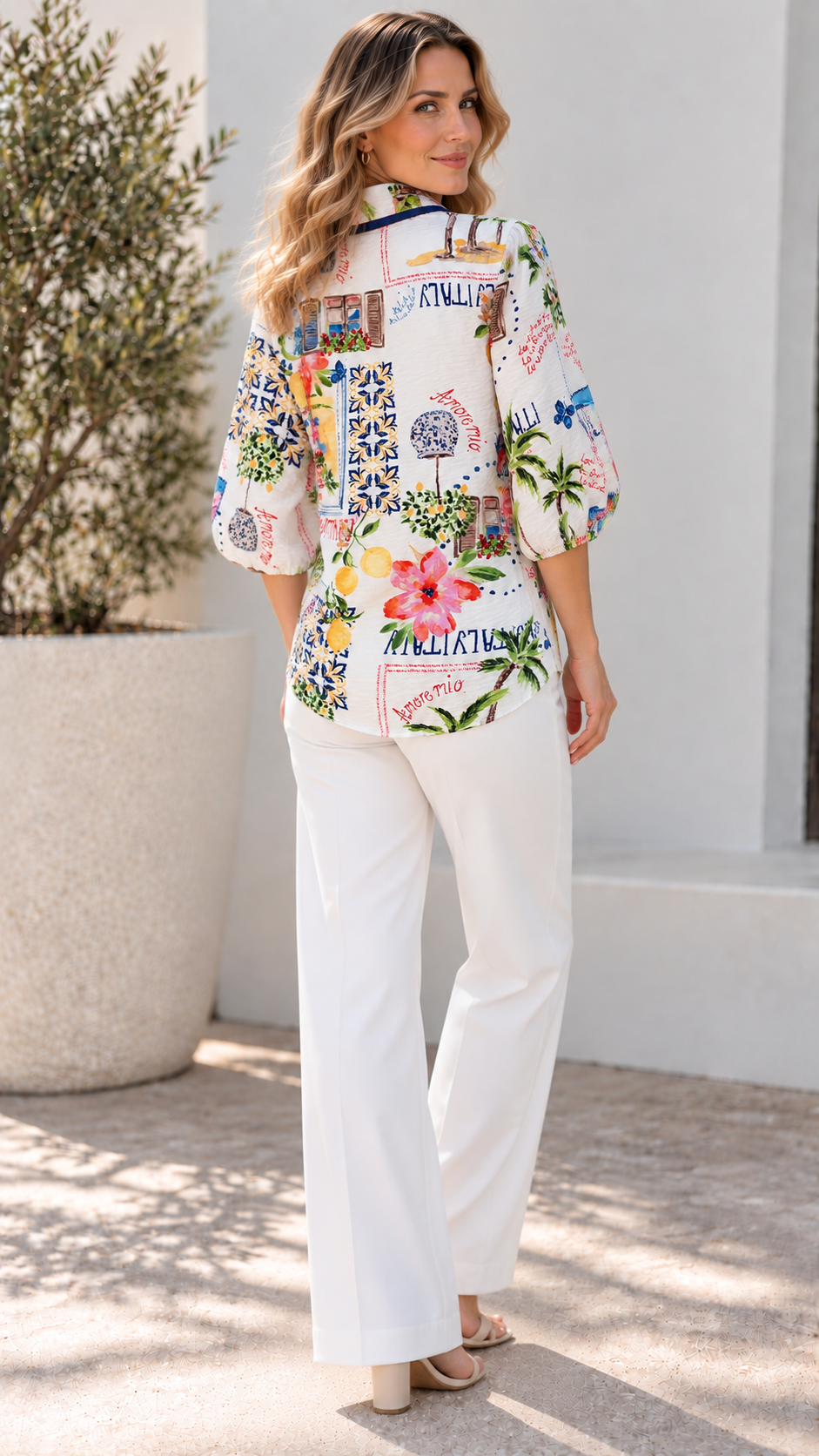 Back view of a white Bella Shirt with colorful Italy print featuring lemons, flowers, and "Amore Mio" text, paired with white trousers.